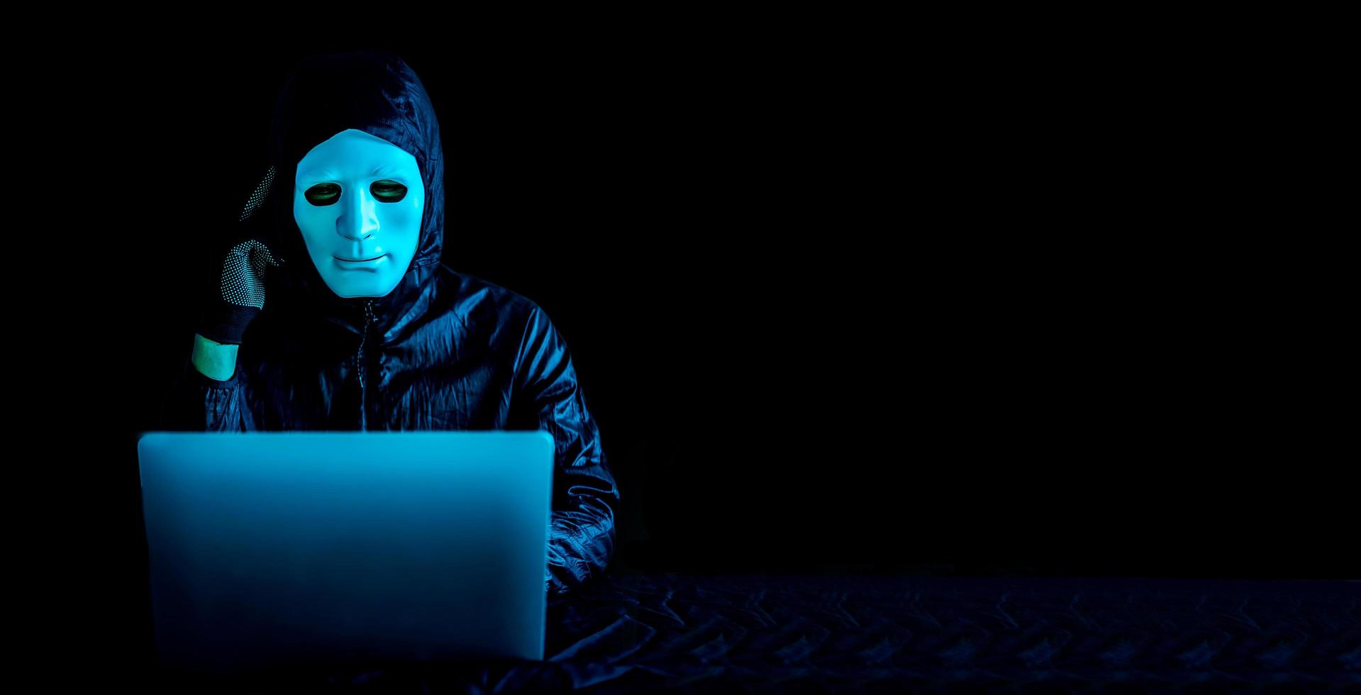 hacker com máscara branca e capuz usando um laptop para navegar na net e rosto sério pensando em questão, terrorista e espaço virtual. conceito de zona insegura, ideia muito confusa foto