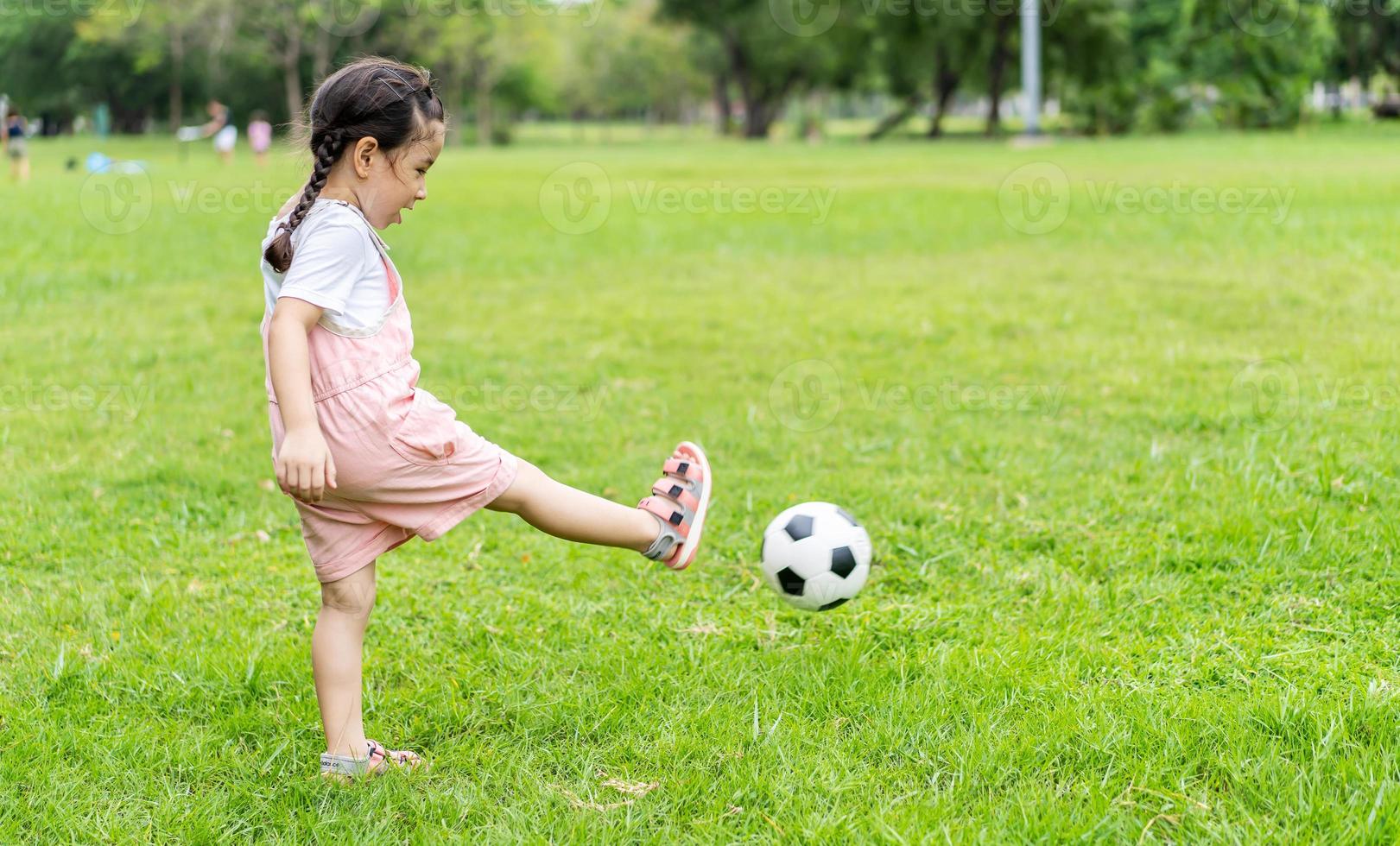 garoto de esportes. garotinha feliz chutando uma bola de futebol, brincadeiras de criança foto