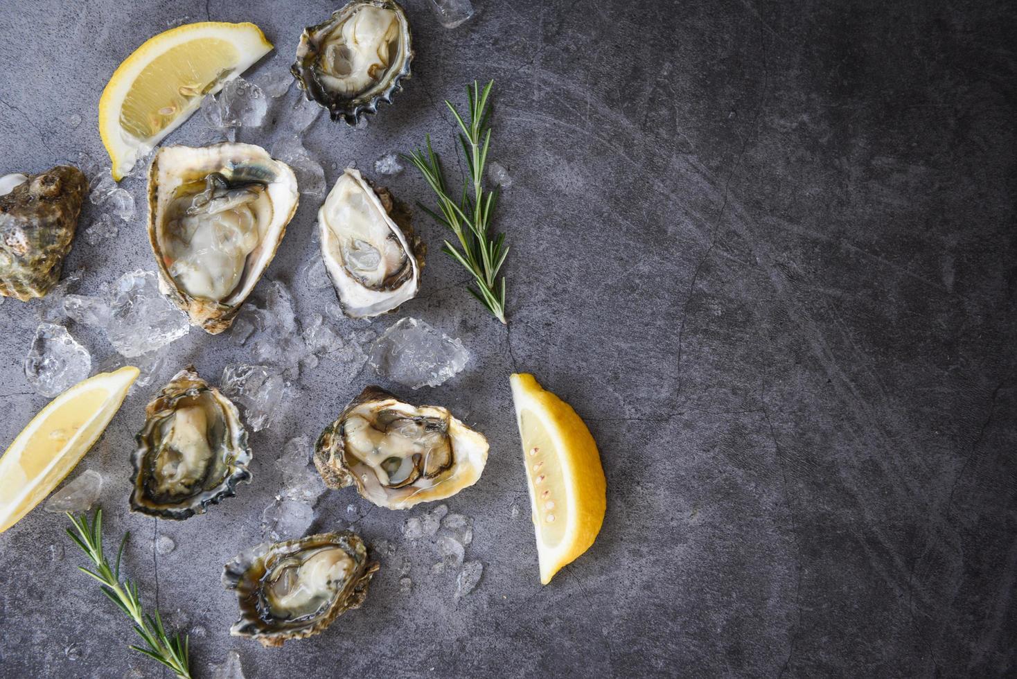 ostras frescas frutos do mar no fundo da placa preta concha de ostra aberta com ervas especiarias limão alecrim servido mesa e gelo frutos do mar saudáveis jantar de ostras cruas no restaurante comida gourmet foto