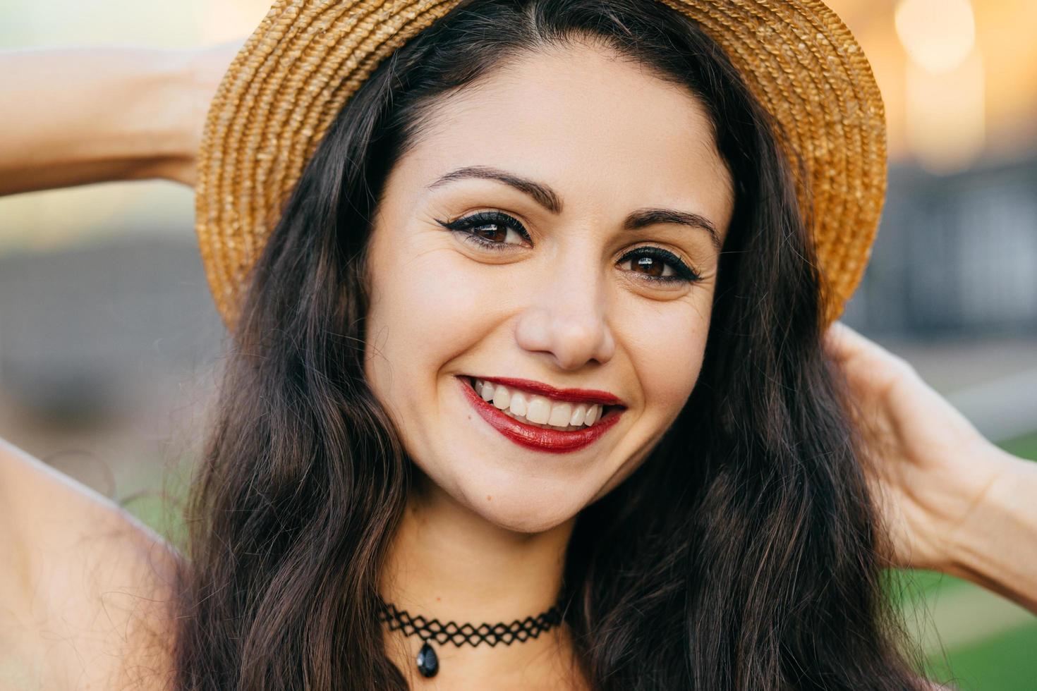 feche o retrato de uma mulher bonita com cabelos escuros, olhos encantadores e sorriso agradável usando chapéu de palha de verão tendo bom humor sentindo relaxamento. modelo feminino atraente com aparência bonita foto