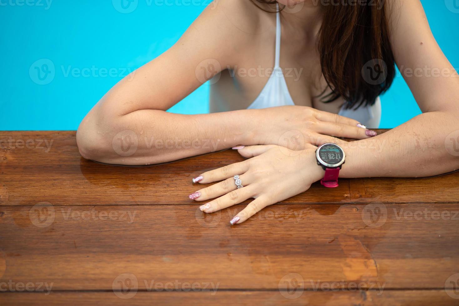 uma mulher usando um relógio smartwatch, ela está relaxando à beira da piscina em casa. foto