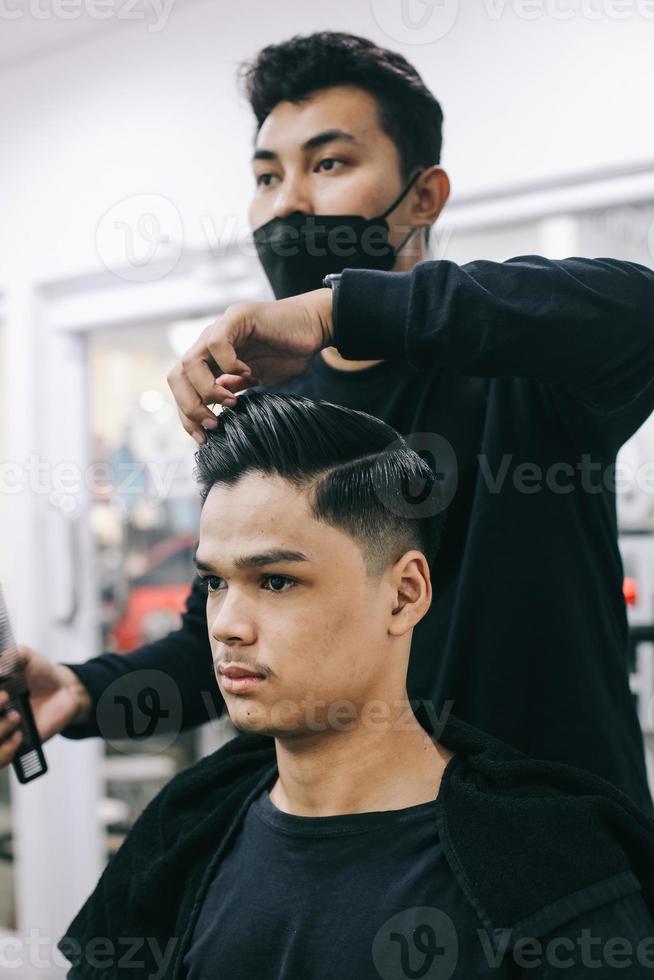 jovem na barbearia. capster penteando o cabelo de seu cliente no salão de cabeleireiro masculino. autocuidado, beleza masculina. barbeiro. foto