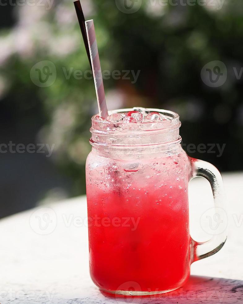 bebida com sabor de água com refrigerante de limão vermelho, bebidas frescas bebidas com gelo em vidro transparente com canudos de papel e plástico na mesa branca foto