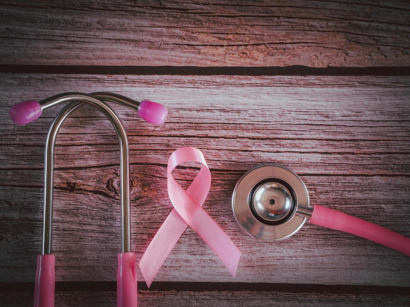 fita rosa e estetoscópio em estilo vintage de mesa de madeira. símbolo do câncer de mama, conceito de cuidados de saúde foto