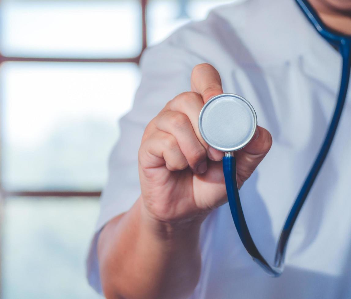 mão de médico de medicina masculina segurando o estetoscópio contra o peito no fundo do hospital. médico pronto para examinar o paciente. conceito de assistência médica e paciente. foto