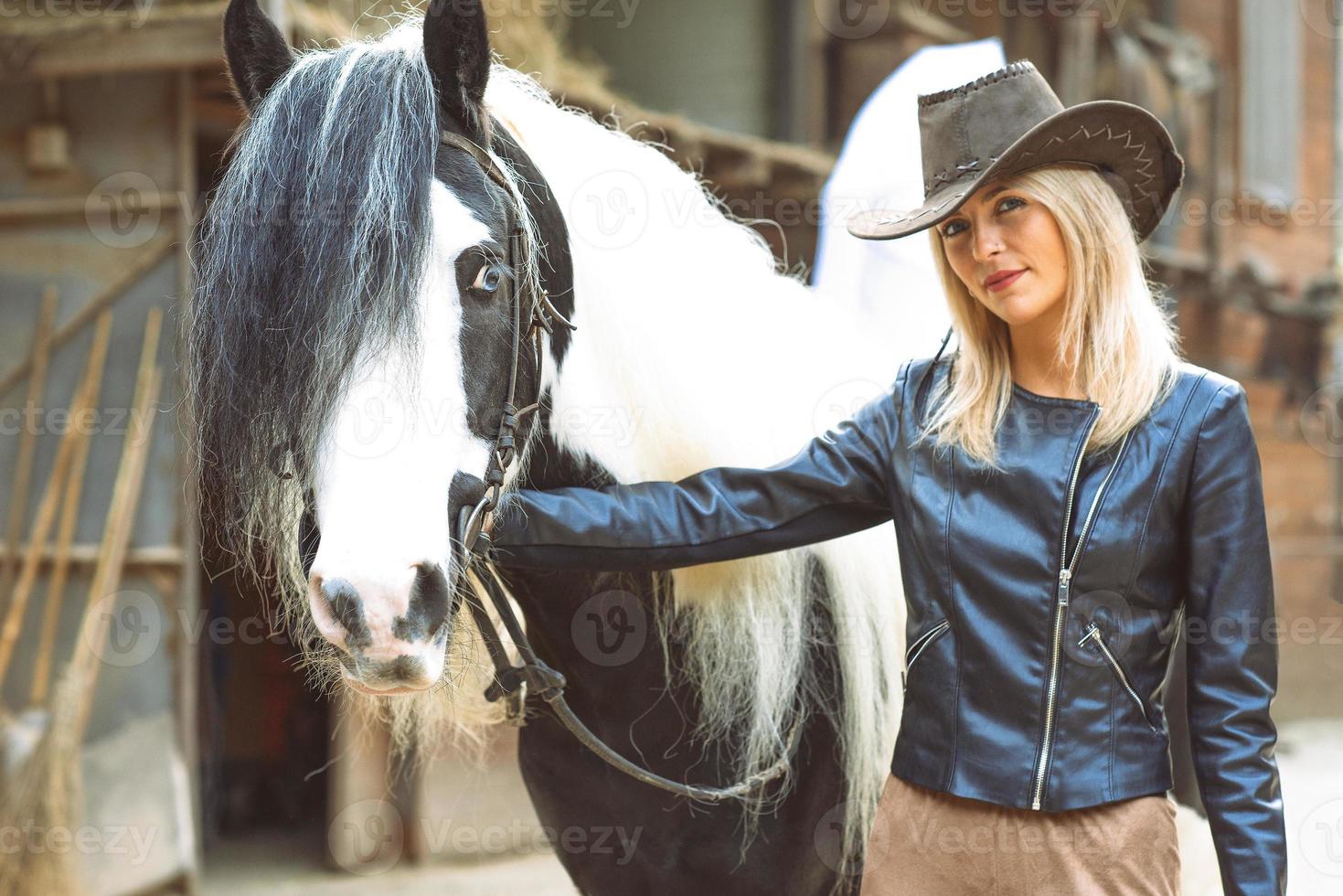 linda mulher loira estilo country com cavalo preto e branco foto