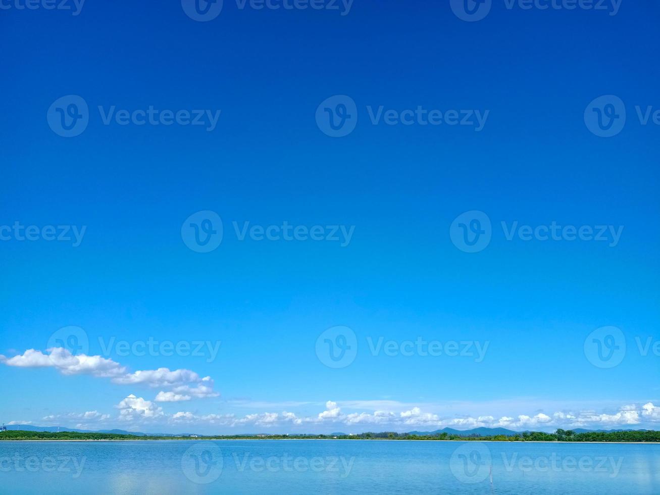 reflexo do céu azul e nuvem branca na superfície do lago com linha de árvore e pequena montanha foto