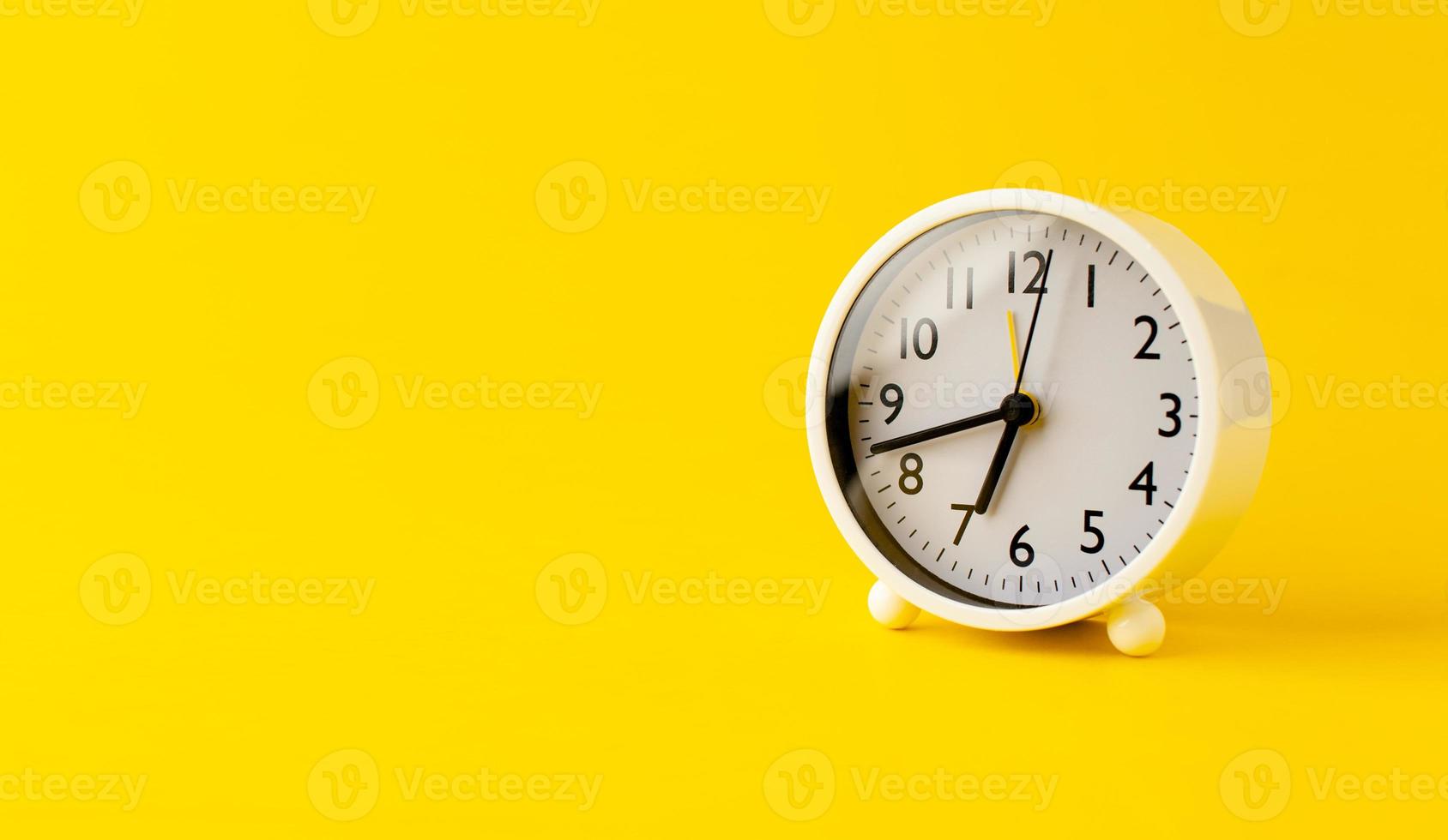 despertador branco em um conceito de tempo de fundo amarelo com palavras-chave tempo de trabalho foto