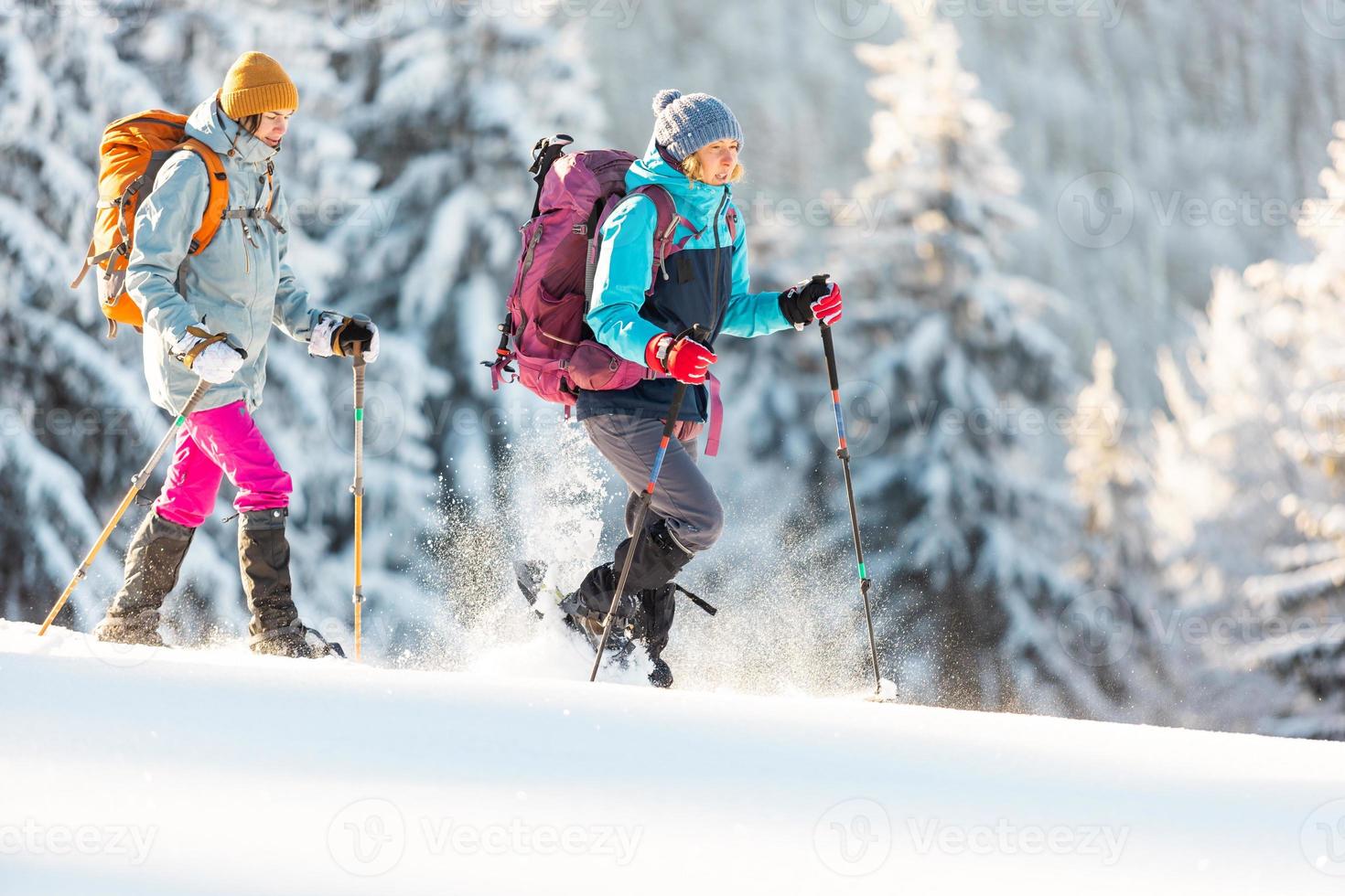 duas mulheres andam com raquetes de neve na trilha da montanha foto