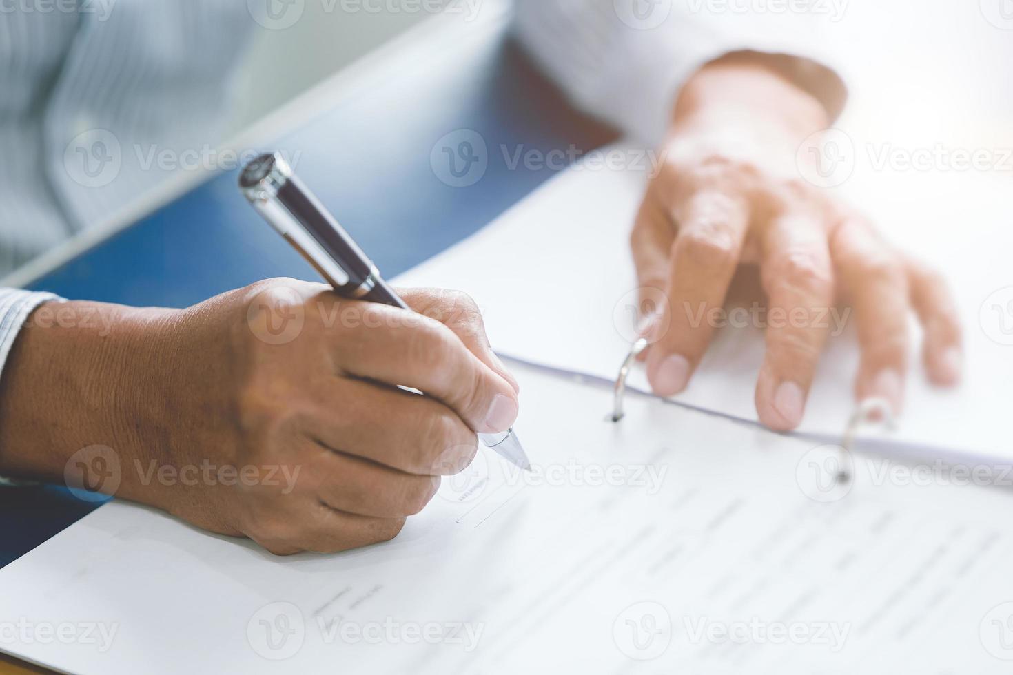 closeup mão mais velha escrevendo papel trabalhando com caneta esferográfica na mesa de escritório. foto