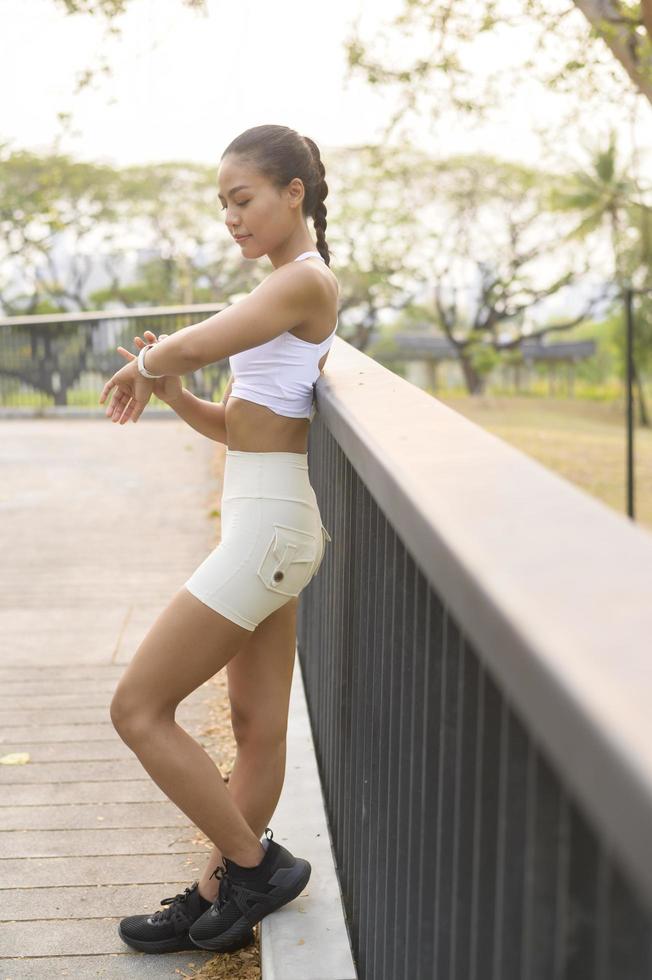 mulher jovem fitness em roupas esportivas usando relógio inteligente enquanto se exercita no parque da cidade, saudável e estilos de vida foto