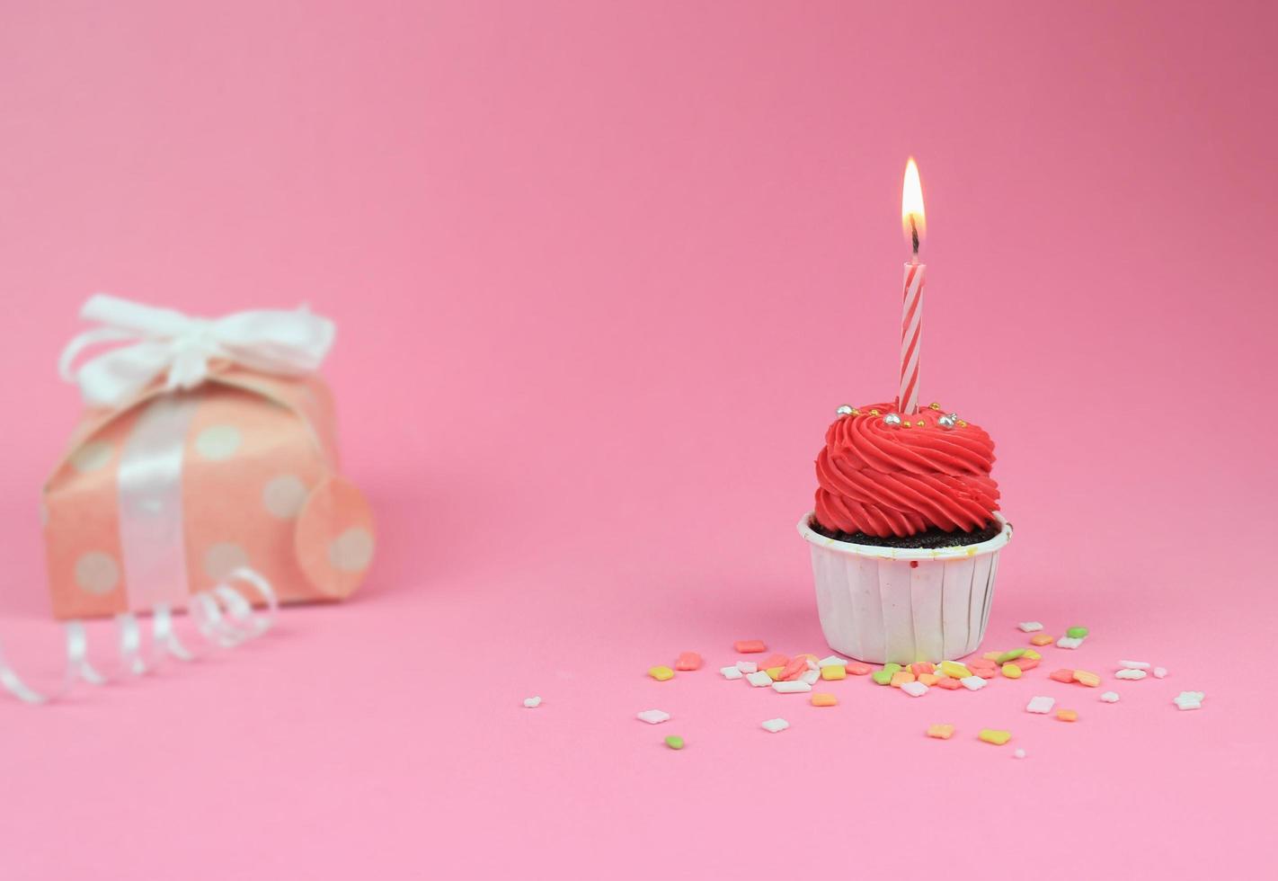 doce cupcake vermelho com vela de laço e caixa de presente em fundo rosa com espaço de cópia. conceito de fundo de festa de aniversário feliz. foto