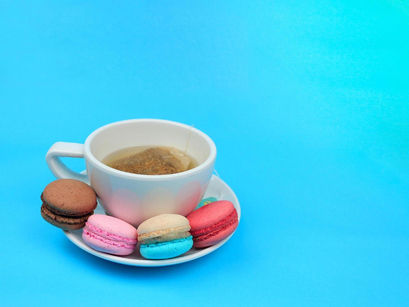 uma xícara de chá com macarons de macarons franceses coloridos bonitos, deliciosa sobremesa doce em fundo azul, conceito de fundo de comida adorável. foto