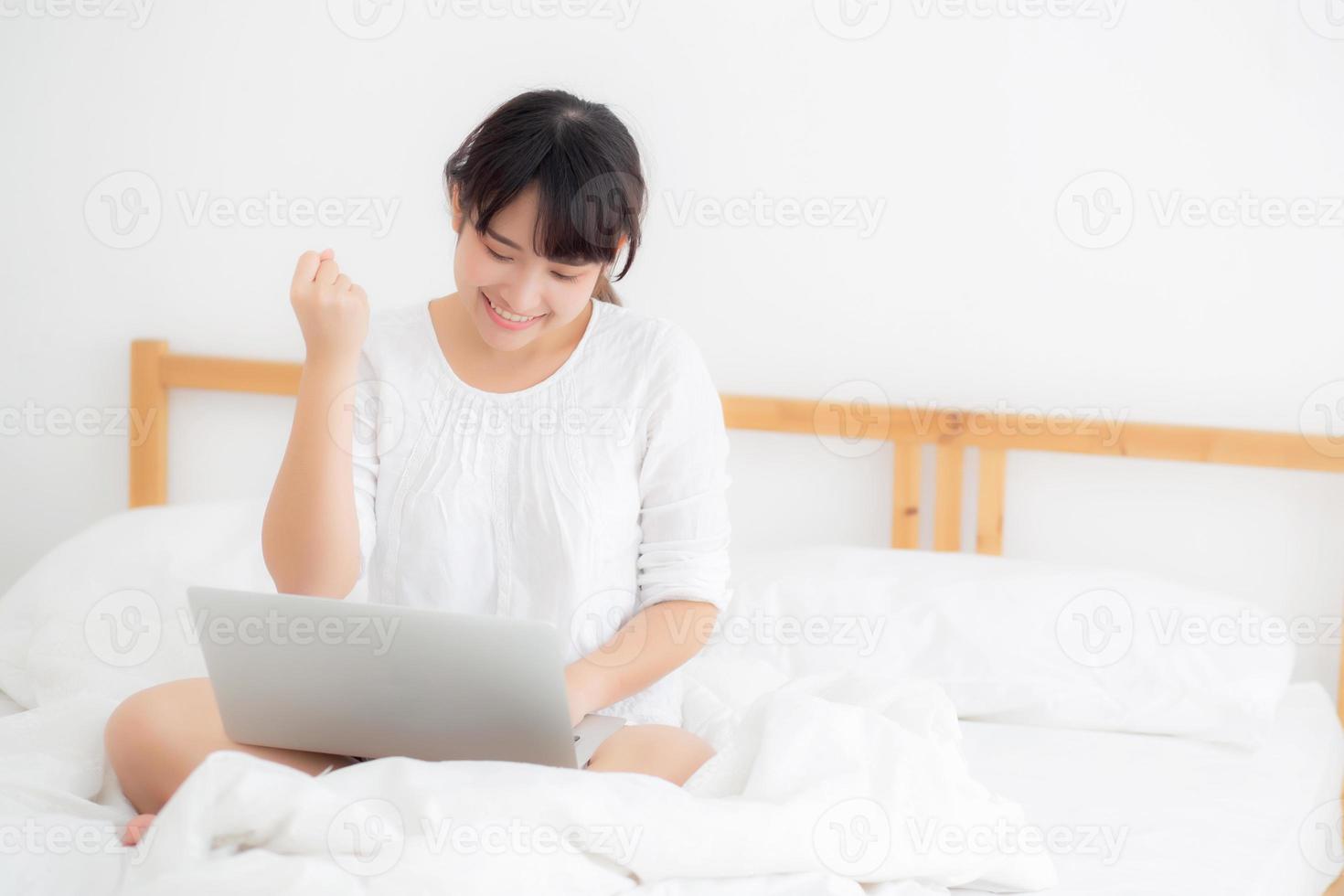 linda de retrato jovem asiático sentado relaxe e lazer com internet de computador portátil on-line na cama no quarto, alegre de garota asiática com gesto feliz e sucesso, conceito de estilo de vida. foto