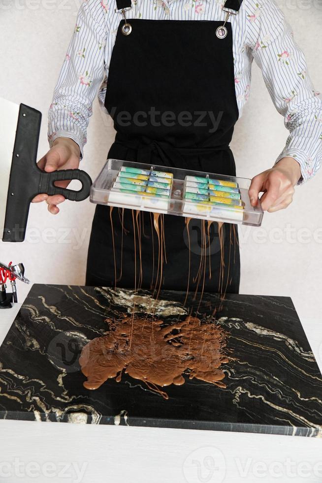 mulher chocolatier faz chocolate na cozinha. ela derrama o resto do chocolate foto