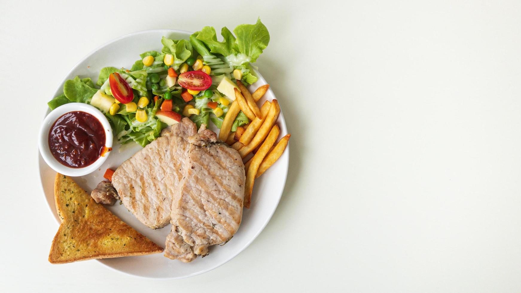 bife de porco com salada, pão e molho de churrasco em um prato branco com espaço de cópia à direita. foto