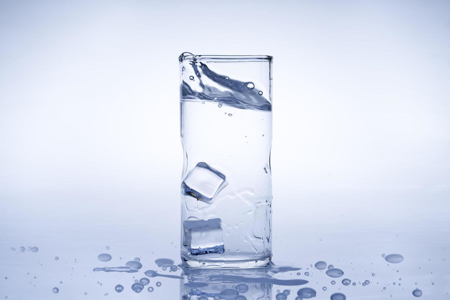 cubo de gelo caiu no copo de água. a água espirrou do vidro transparente. conceito fresco foto