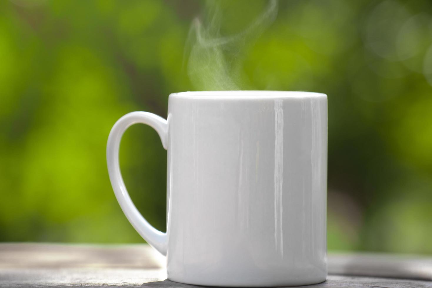 caneca de café cerâmica branca no chão de madeira, fundo de bokeh de árvore verde. efeito de foco suave focus.shallow. foto