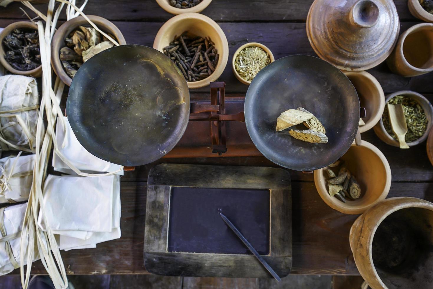 profundidade rasa do tiro de campo do equilíbrio de peso de balanças antigas, preparação natural para medicina tradicional com ervas tailandesas secas foto