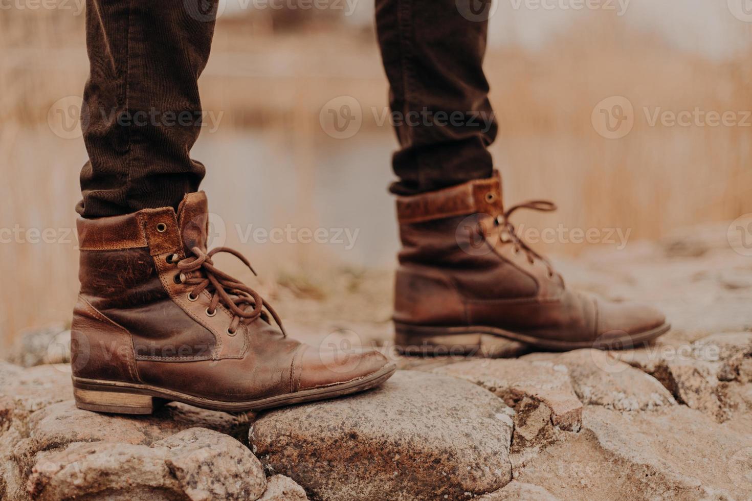 foto recortada de homem irreconhecível usa sapatos velhos, anda ao ar livre, fundo desfocado. botas em pedras. conceito de moda