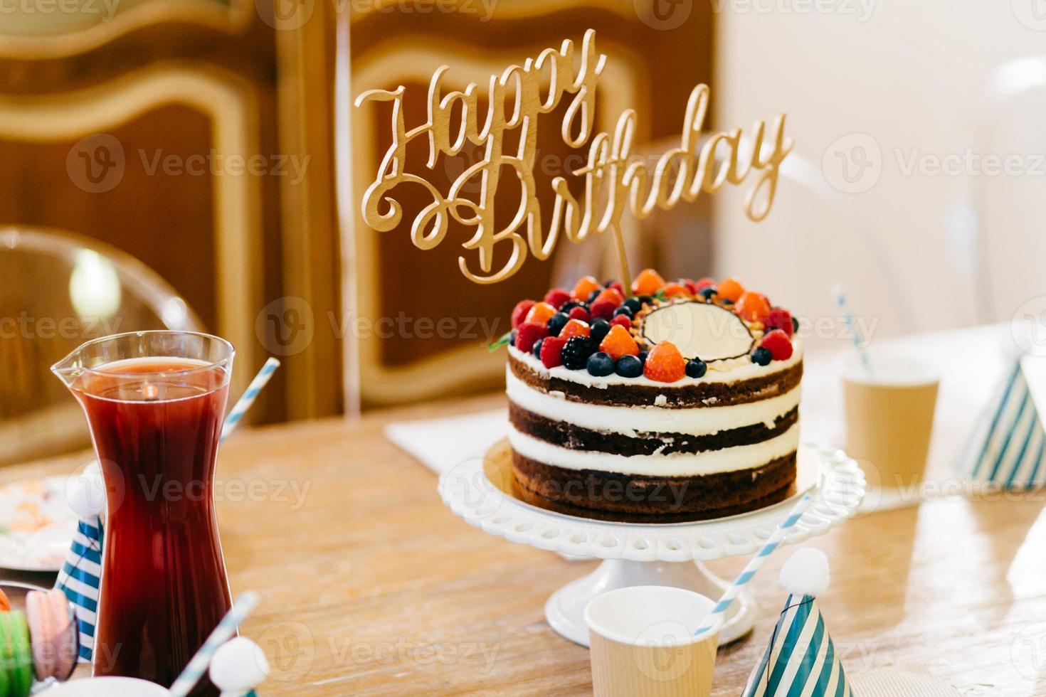 delicioso bolo de aniversário na mesa de madeira com copos e compota. mesa de aniversário. conceito de preparação e celebração. retrato de suprimentos para festa de aniversário. mesa servida para o jantar de aniversário. decorações foto