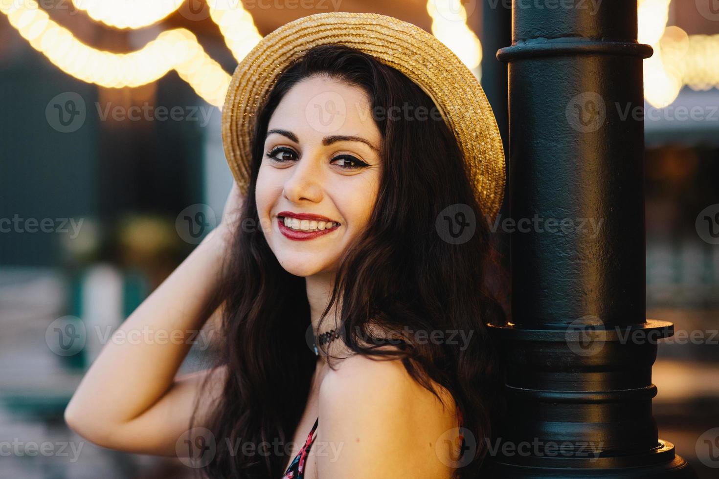 feche o retrato de uma bela mulher com olhos escuros e atraentes, sorrindo suavemente para a câmera enquanto posava dentro de casa na cafeteria. romântica jovem atraente com maquiagem usando chapéu de palha de verão foto