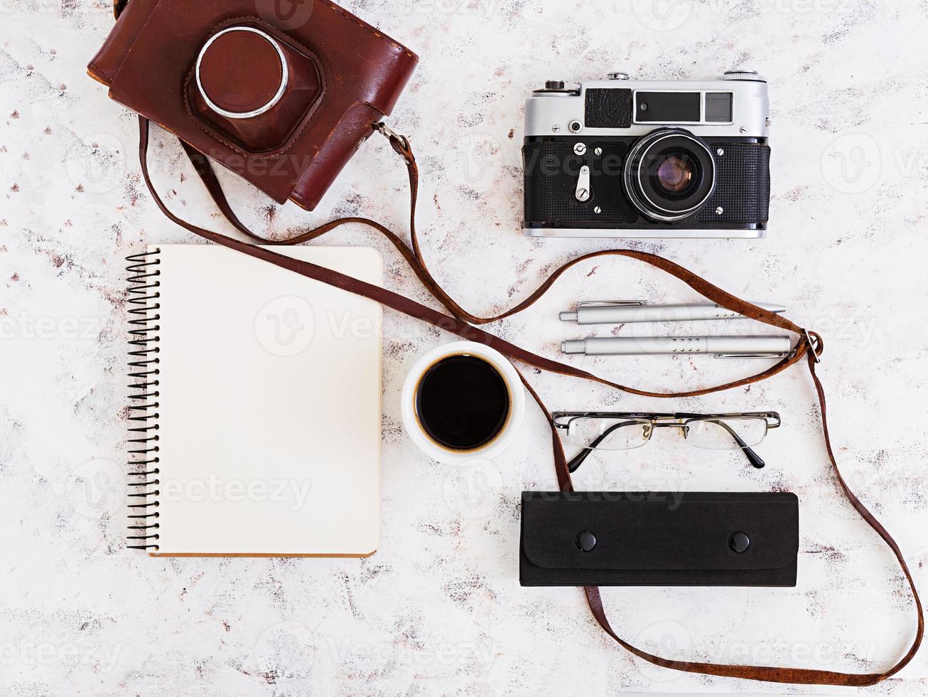 mesa de escritório plana, vista superior. espaço de trabalho de mesa com câmera retro, diário, caneta, óculos, estojo, xícara de café em fundo branco. foto