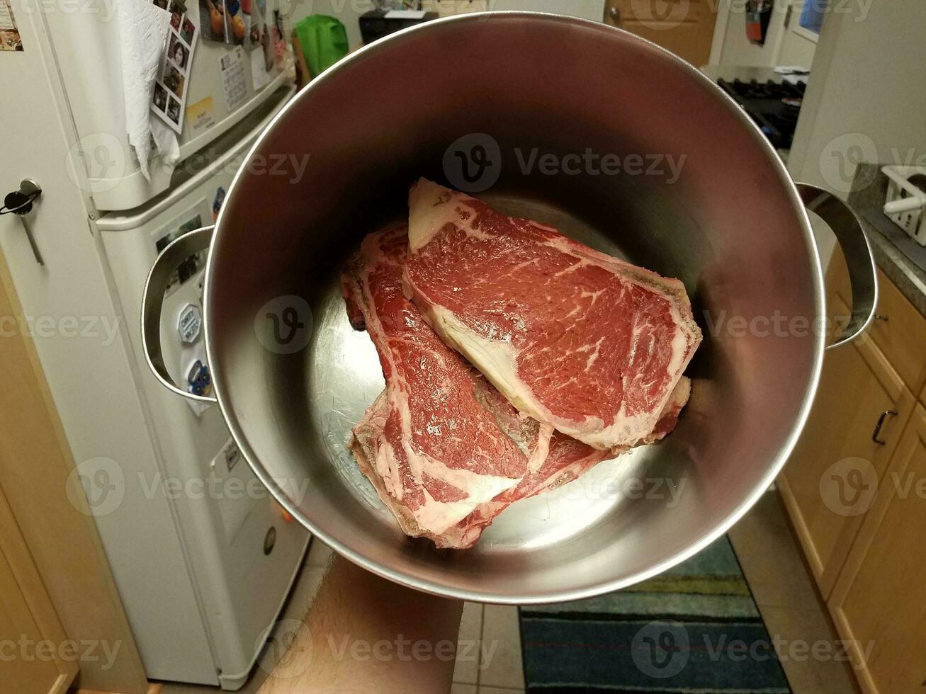 mão segurando bife em panela de metal na cozinha foto