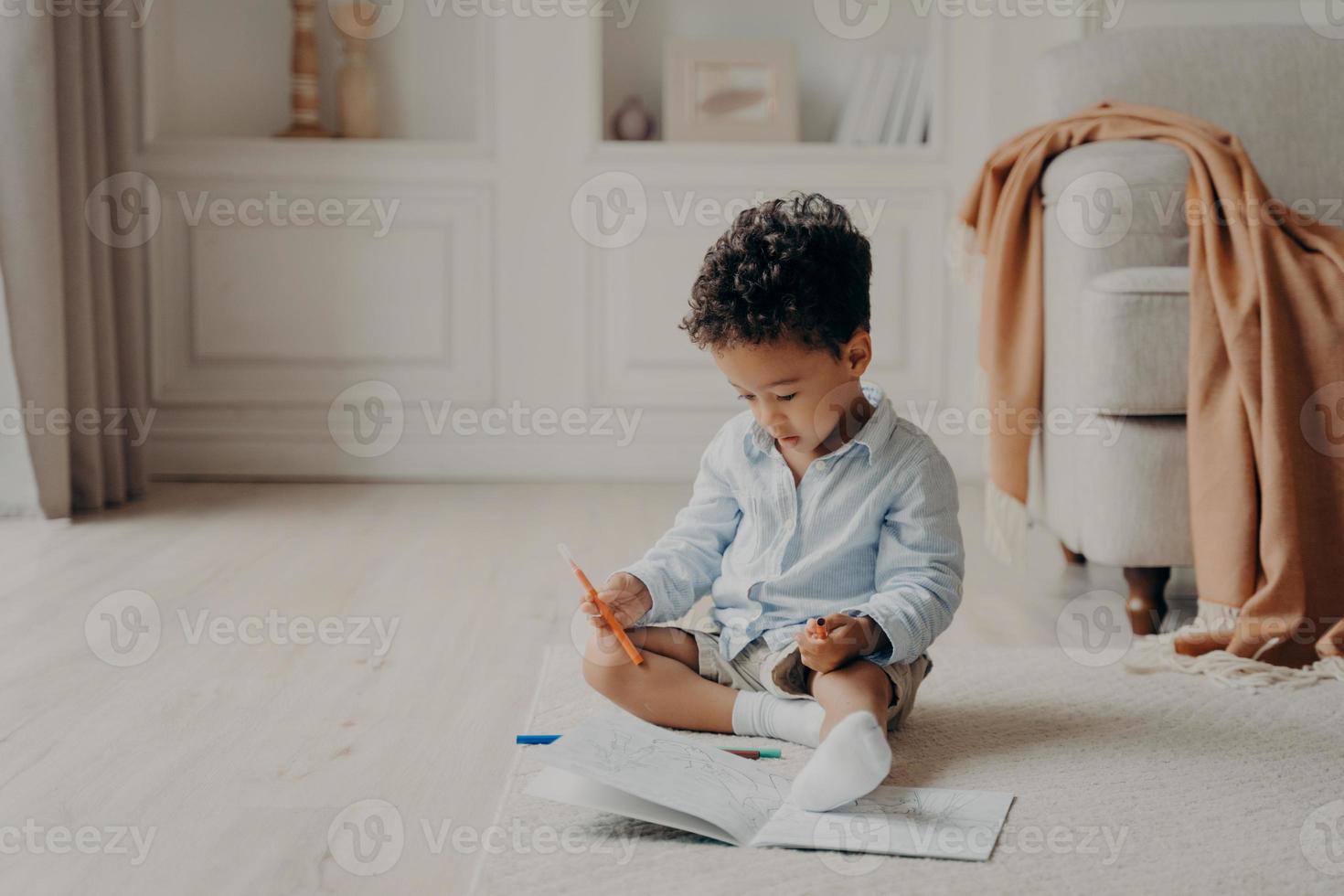pequeno menino mulato afro encaracolado com livro de colorir em casa foto