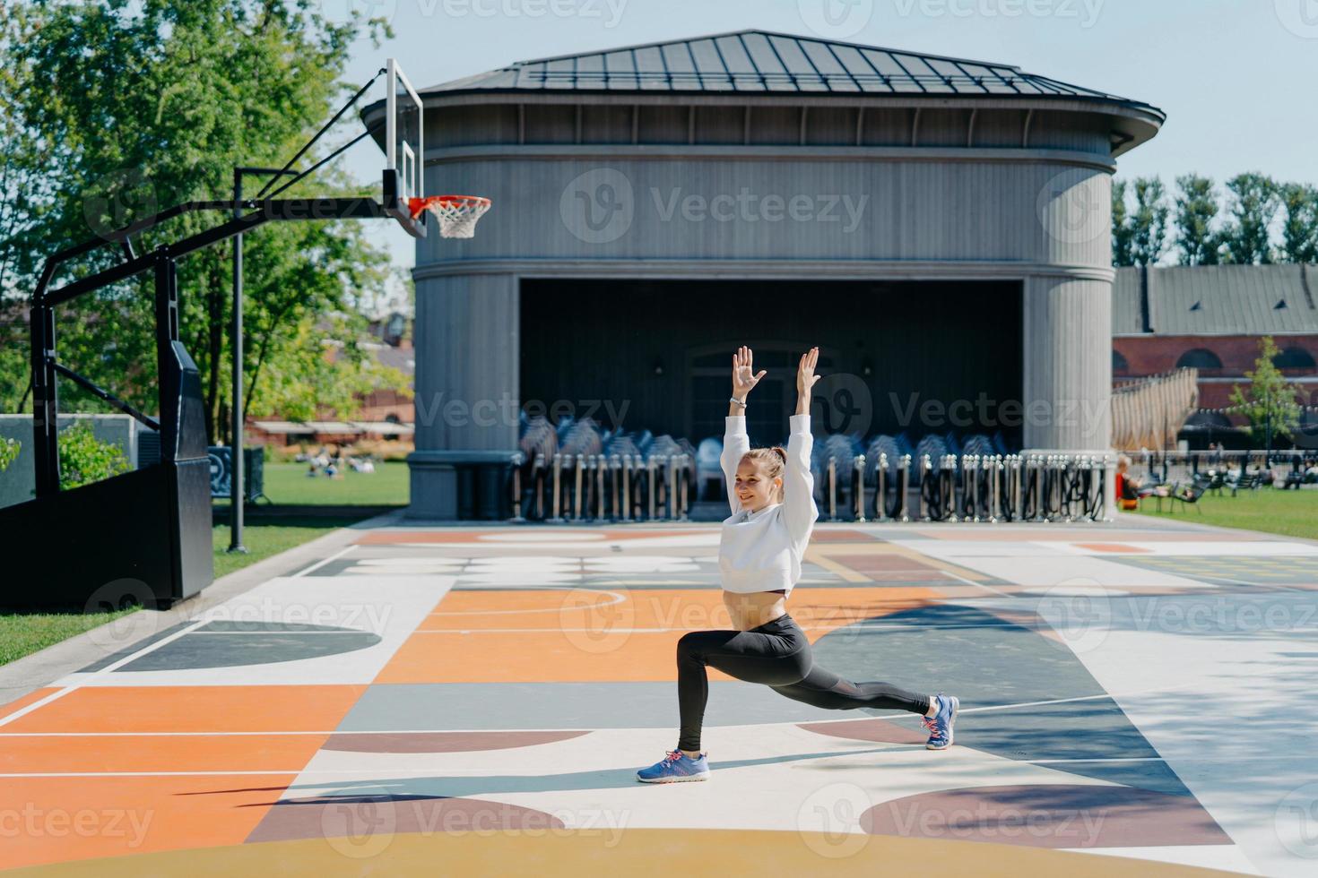 rotina de treino pessoal. mulher atlética faz exercícios físicos ao ar livre mantém os braços levantados aquece antes de correr vestido com poses de desgaste ativo na quadra de basquete. flexibilidade e condicionamento físico foto