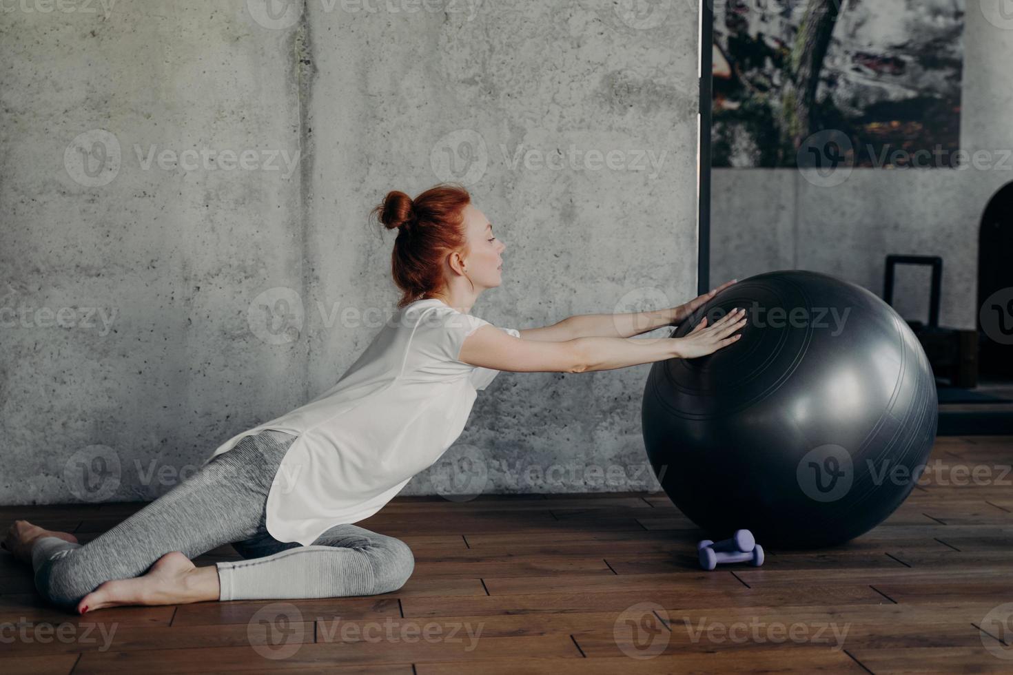 jovem alegre atlética com cabelo vermelho exercitando dentro de casa com fitball foto