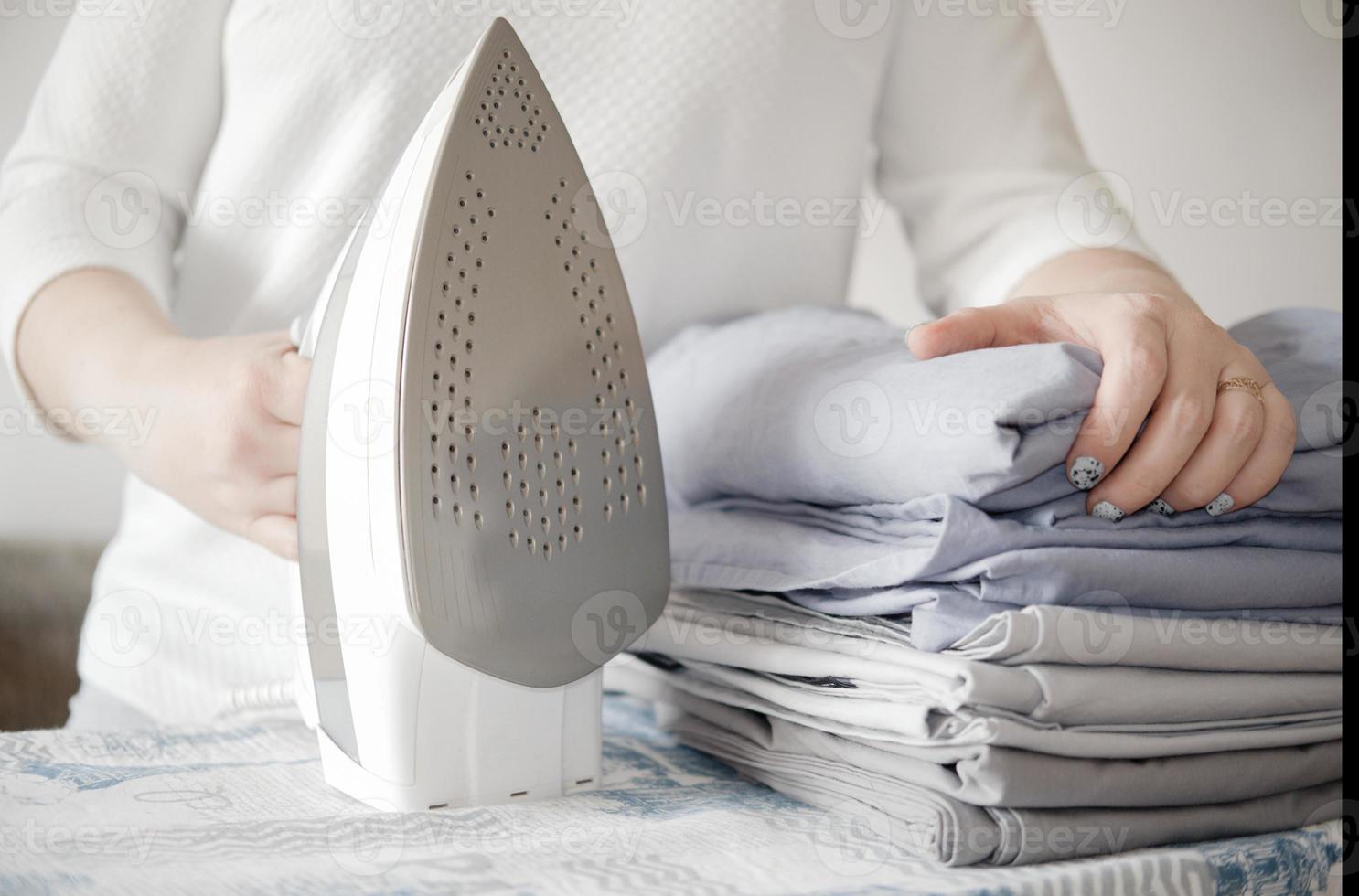 mulher segurando pilha de roupas de cama ou roupa de cama e ferro. conceito de trabalho em casa. foto