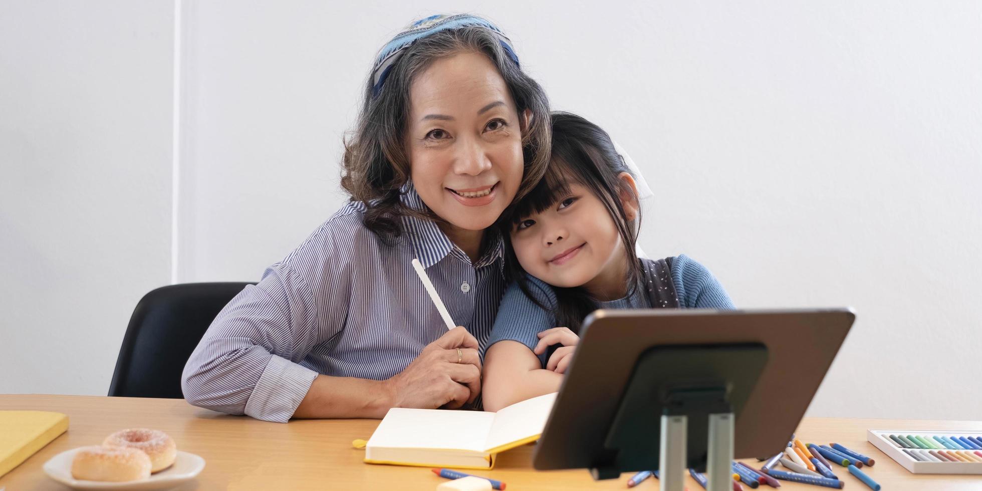 avó sorridente e neta bonitinha assistindo desenhos no laptop juntos e olhe para a câmera vovó feliz jogando ou fazendo compras on-line com as meninas no computador. foto