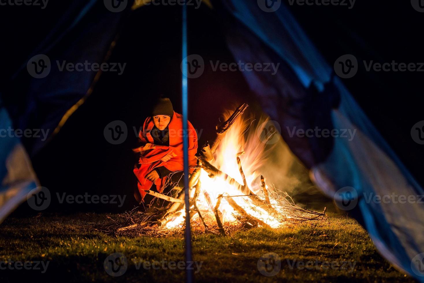 jovem perto da fogueira de acampamento com cobertor foto