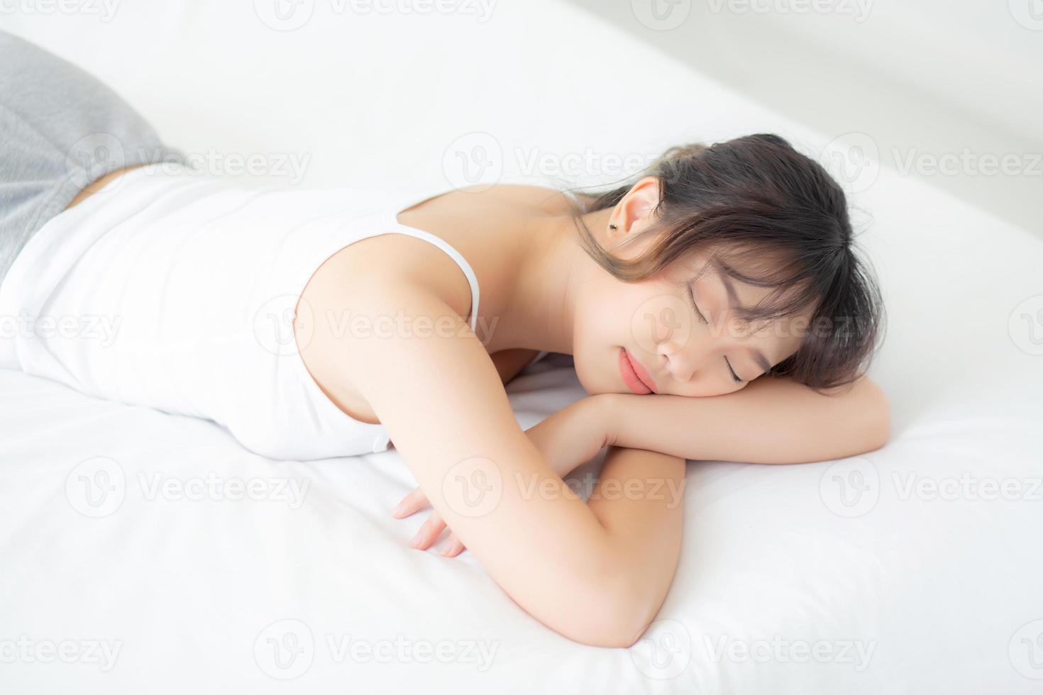 bela jovem asiática sorri dormindo deitada na cama com lazer confortável e feliz no quarto, beleza ásia menina bem-estar com relaxar e fresco para o conceito de saúde. foto