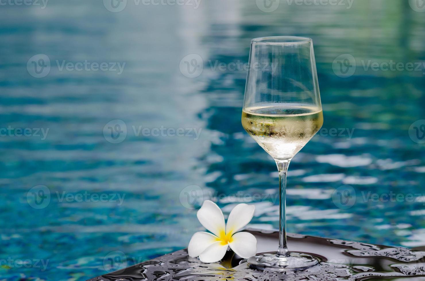 um copo de vinho branco com flor de frangipani no fundo da piscina. conceito de bebida de férias e verão. foto