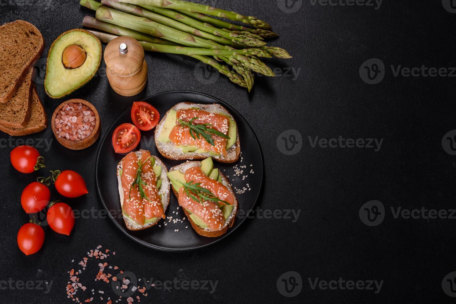 sanduíche de torrada com manteiga, abacate e salmão, decorado com rúcula e sementes de gergelim, sobre fundo de pedra preta foto