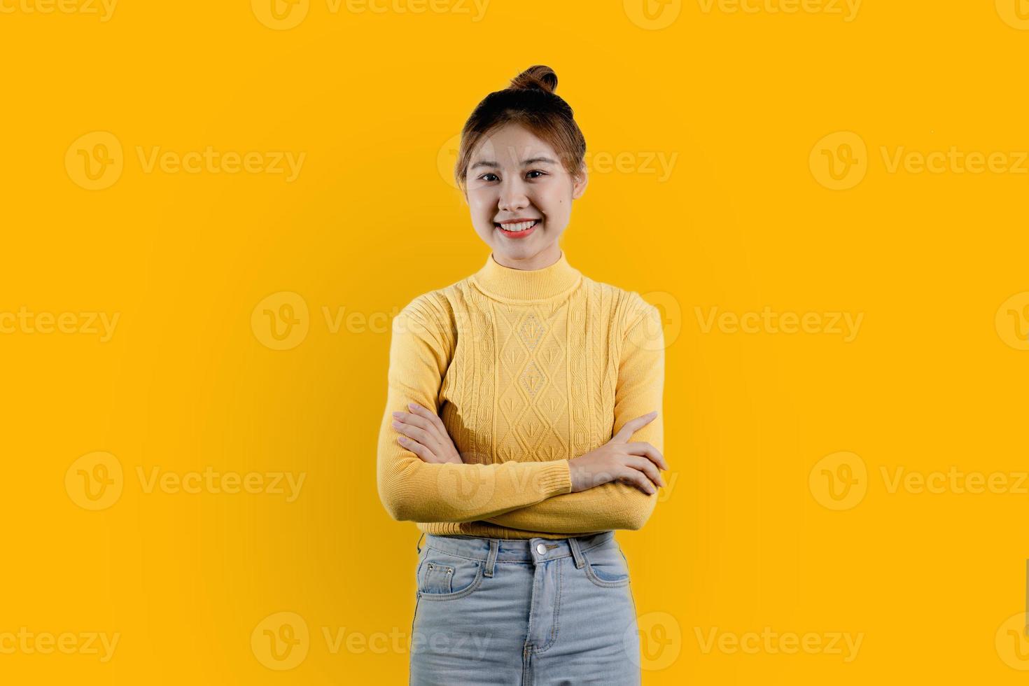 retrato de uma linda mulher asiática em uma camisa amarela em pé com os braços cruzados e sorrindo. conceito de retrato usado para propaganda e sinalização, isolado sobre fundo amarelo, copie o espaço. foto