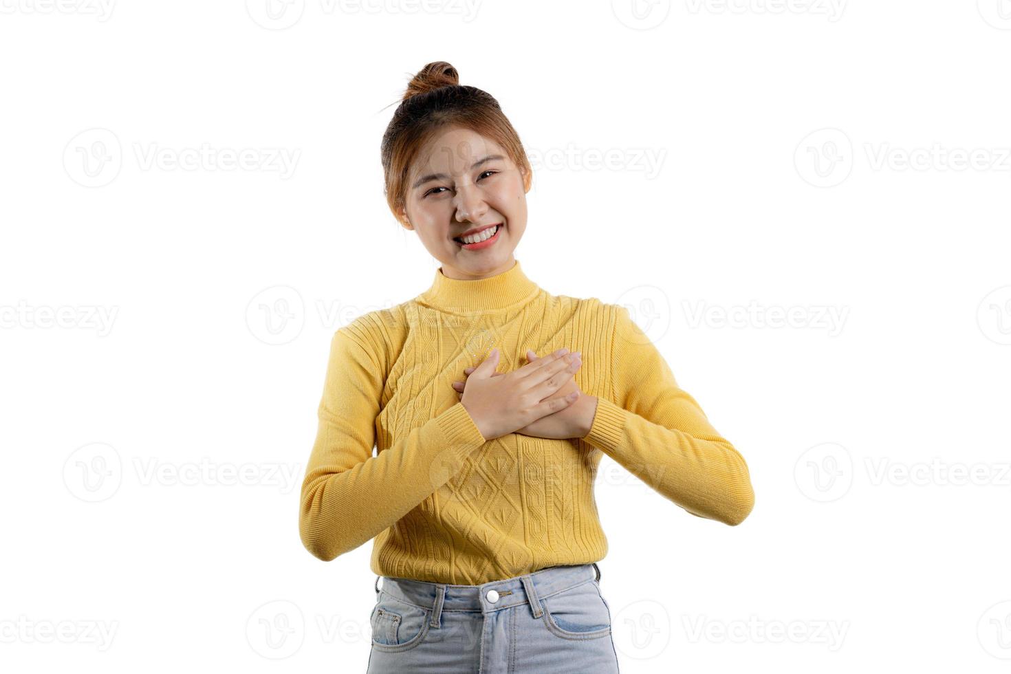 um retrato de uma linda mulher asiática em uma camisa amarela em pé com as duas mãos no coração. conceito de retrato usado para propaganda e sinalização, isolado sobre o fundo em branco, copie o espaço. foto