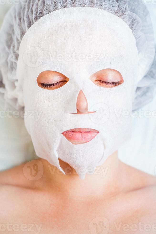 mulher relaxante no salão spa, aplicação de máscara facial branca foto