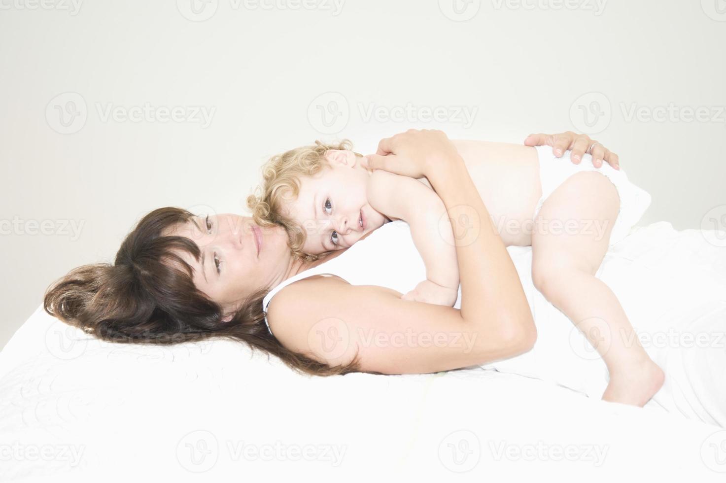 bebê deitado em cima da mãe na cama foto