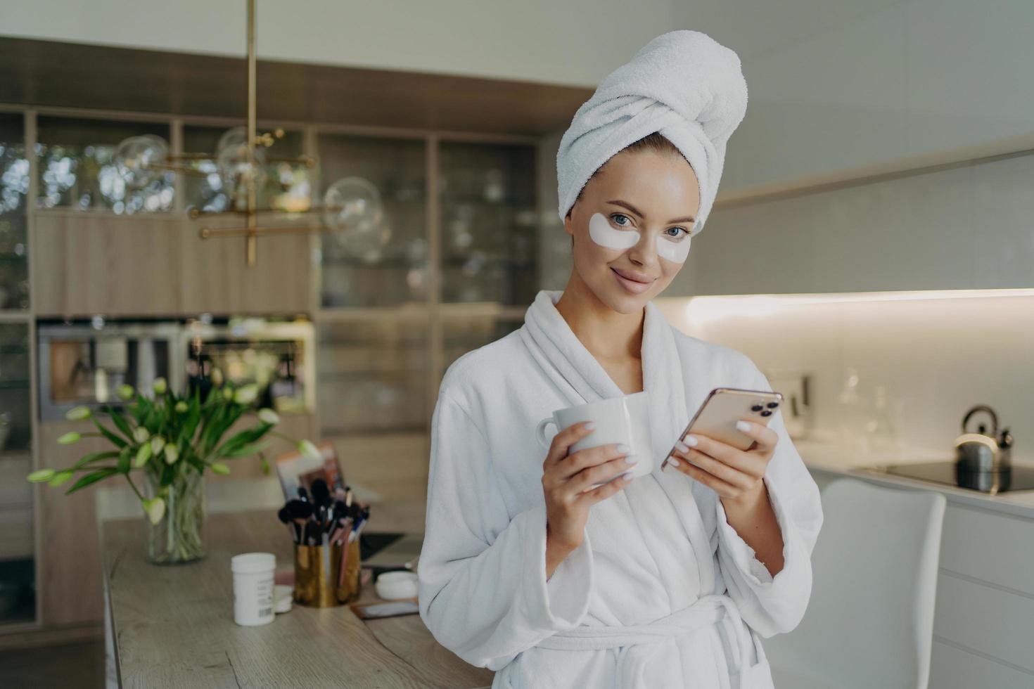 mulher feliz em roupão de banho e toalha na cabeça relaxando com uma xícara de chá ao fazer procedimentos cosméticos em casa foto