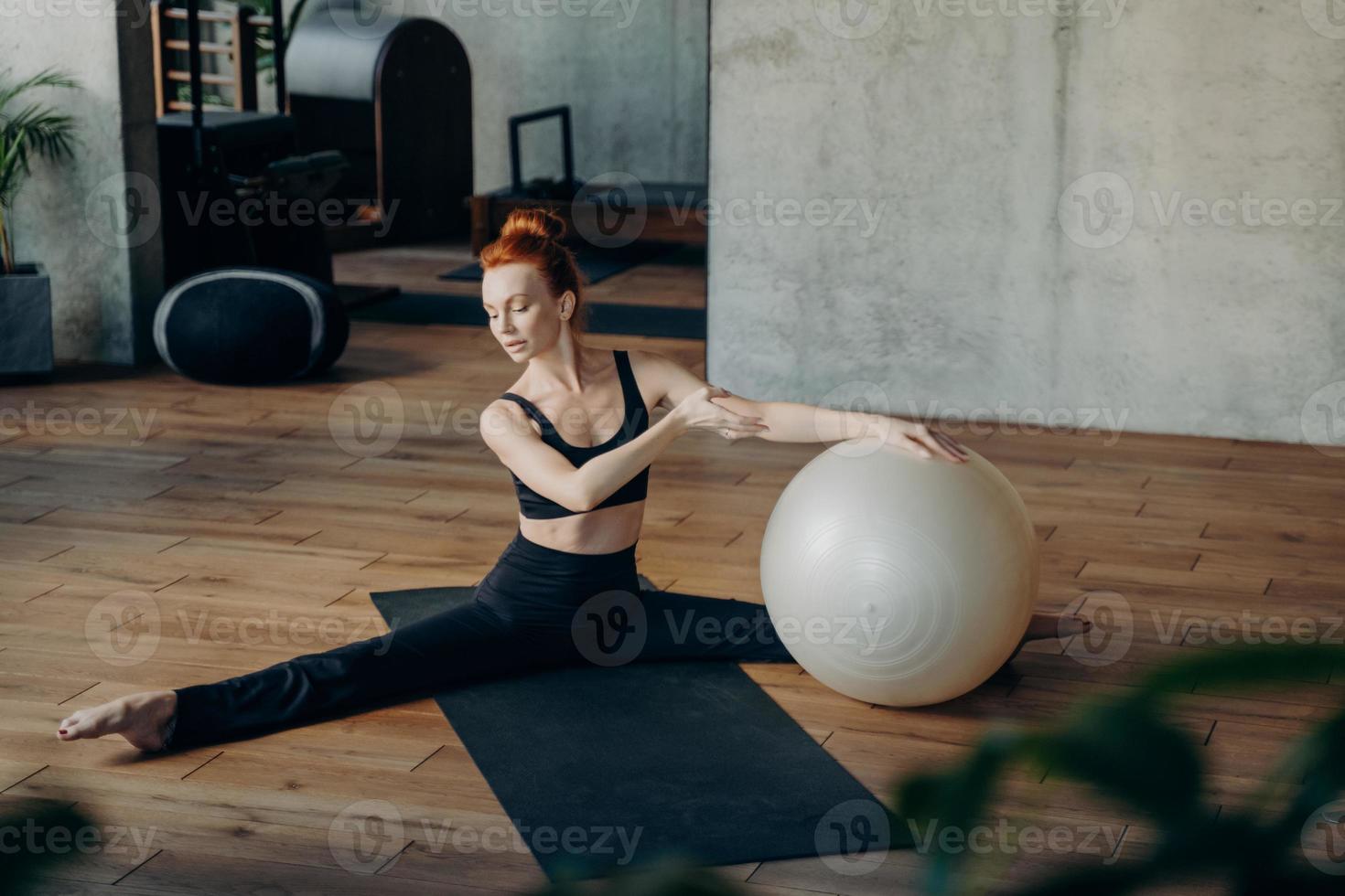 jovem em posição dividida exercitando com fitball no estúdio de fitness foto