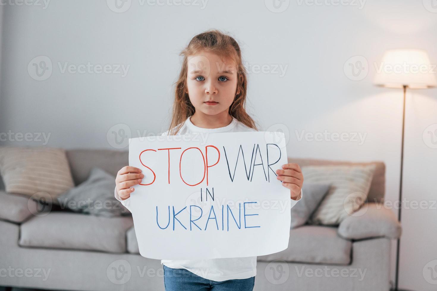 menina de pé em casa e segurando o banner com parar a guerra no texto da ucrânia foto