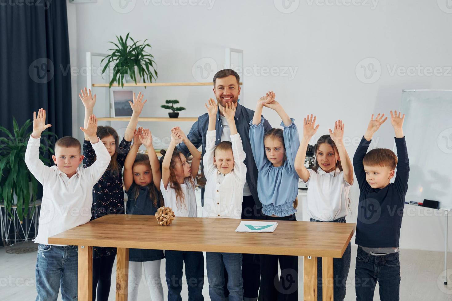 em pé e posando. sorrindo juntos. grupo de alunos de crianças em sala de aula na escola com professor foto