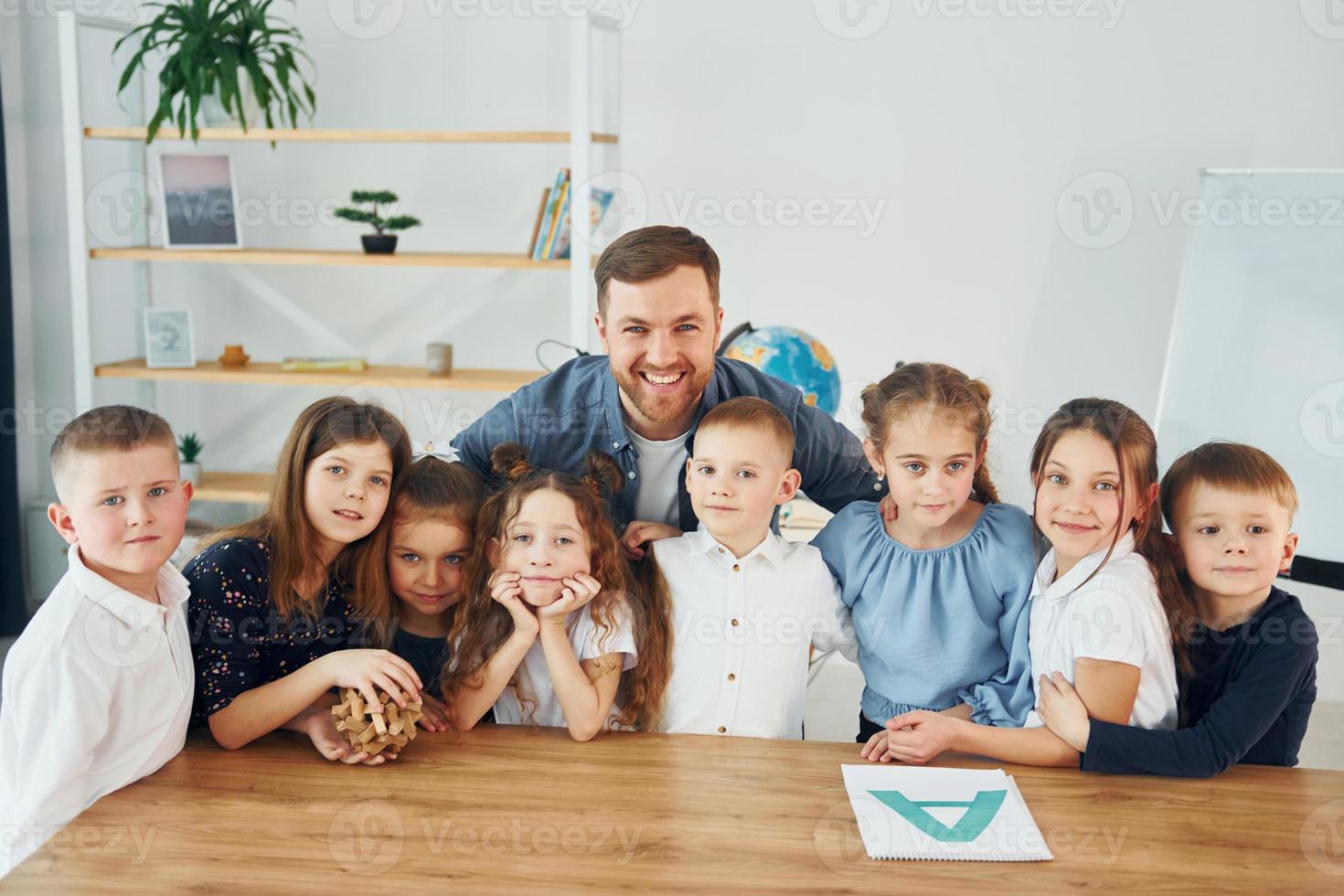 em pé e posando. sorrindo juntos. grupo de alunos de crianças em sala de aula na escola com professor foto