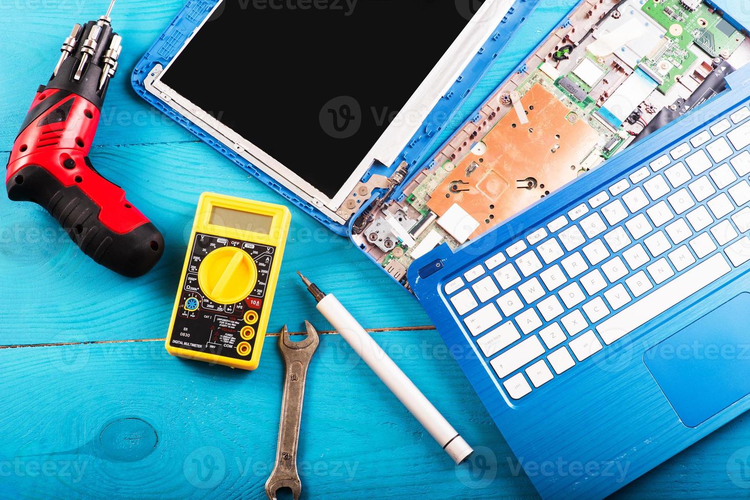 assistente repara laptop com ferramentas e mãos na mesa de madeira azul. vista do topo foto