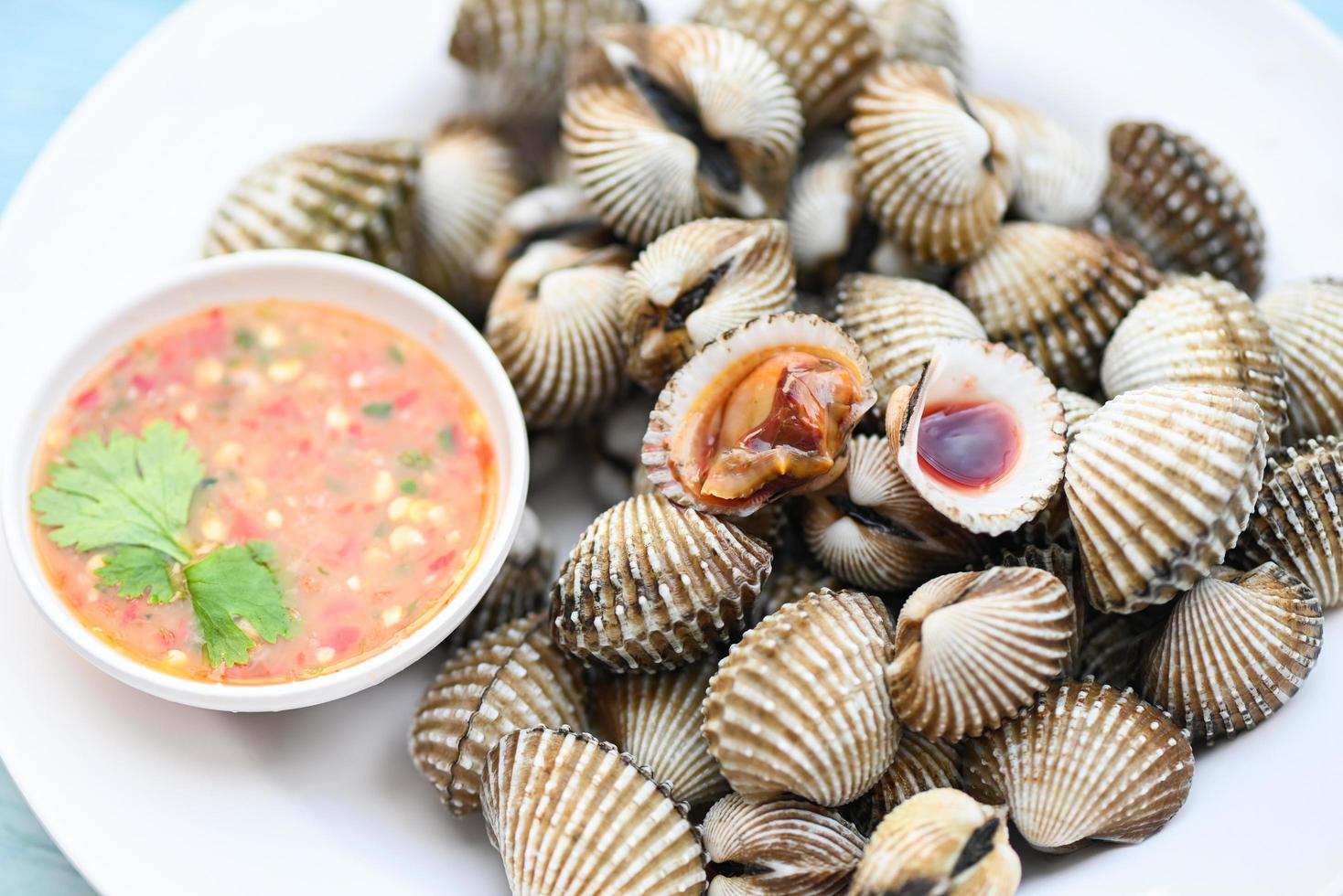 berbigão na chapa branca com molho de frutos do mar no fundo da mesa, marisco cru fresco sangue berbigão oceano marisco gourmet no restaurante foto