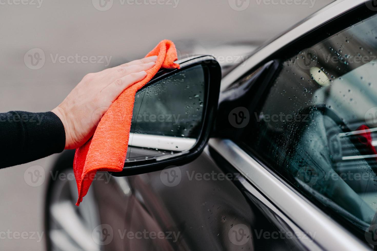 close-up da mão do homem limpando a água no carro preto com pano de microfibra. foco no espelho lateral automático. autoatendimento transporte foto