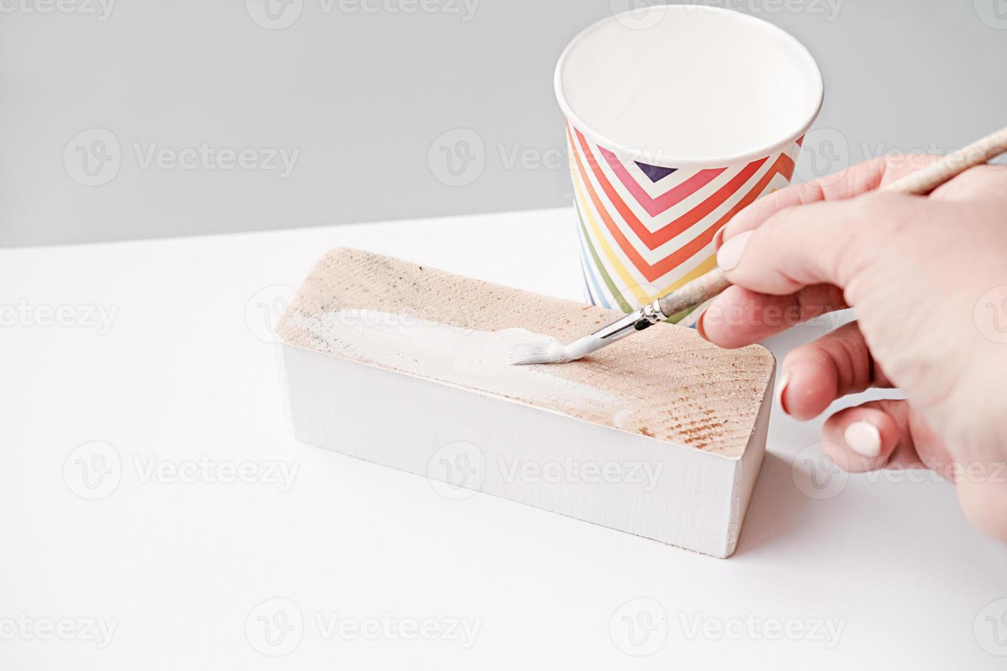 mão feminina pintando bloco de madeira com tinta branca foto